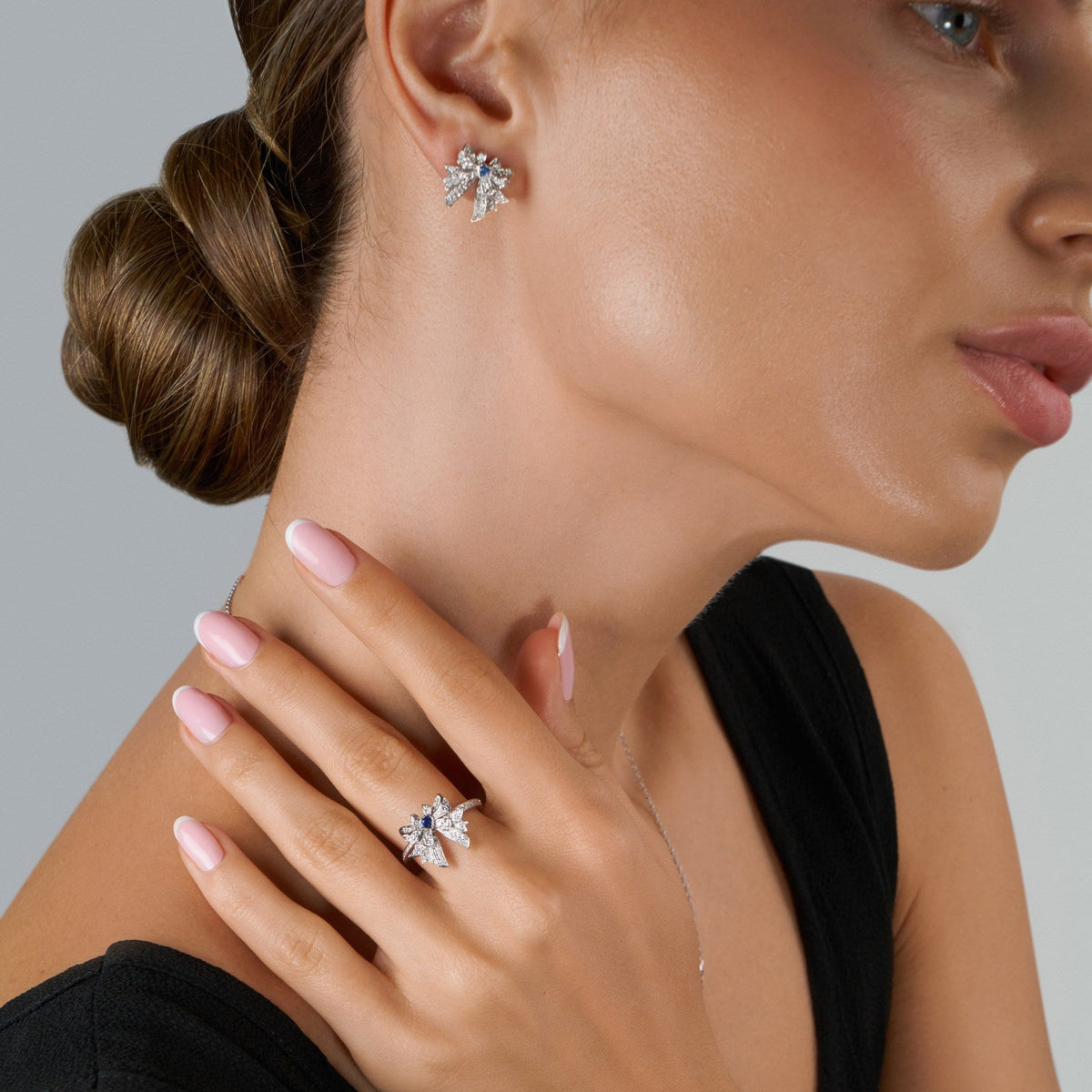 Woman wearing diamond jewelry including earrings, ring, and bracelet on a neutral background