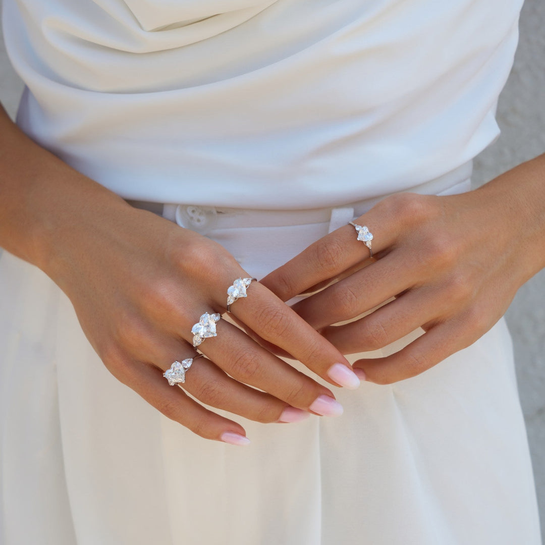 Close-up of hands wearing multiple diamond rings on a neutral background
