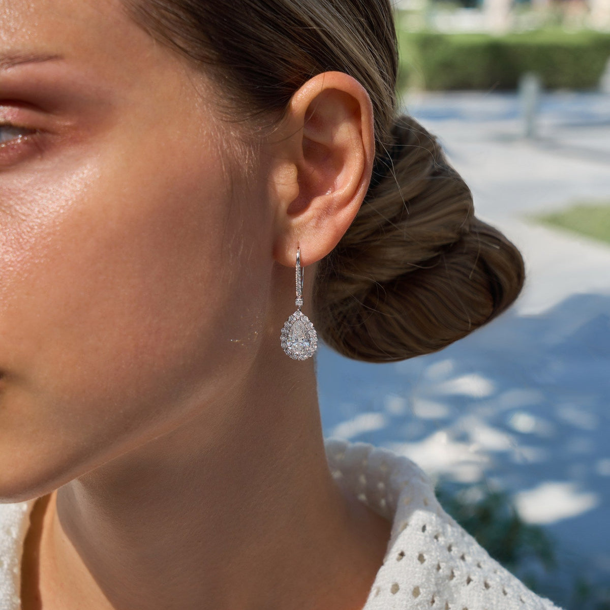 Close up of a woman wearing diamond earrings with a blurred outdoor background