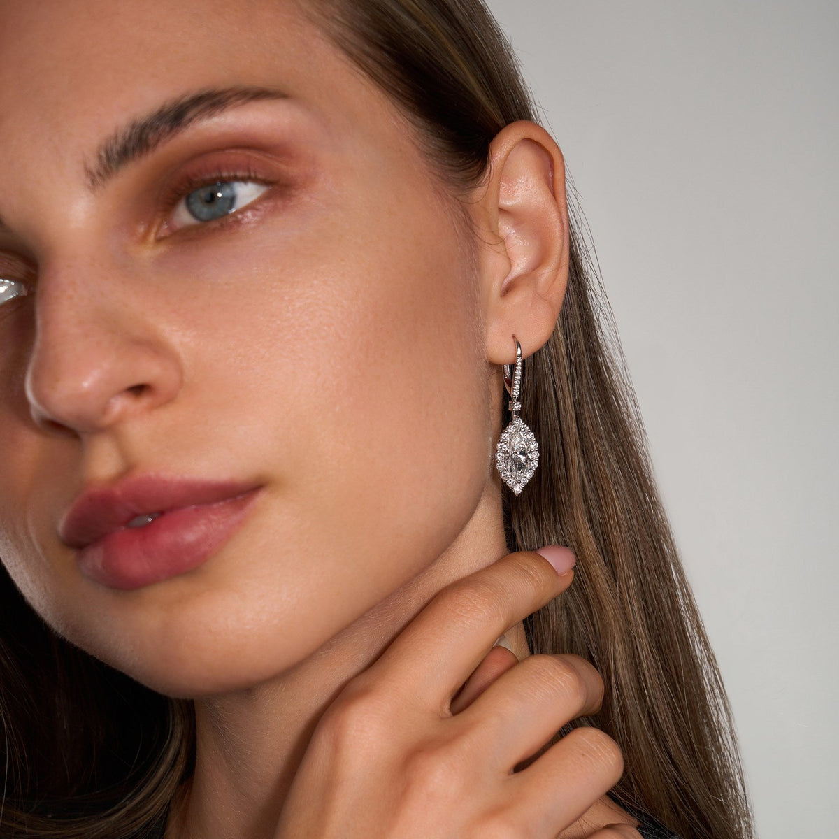Close up of a woman wearing diamond earrings with a neutral background